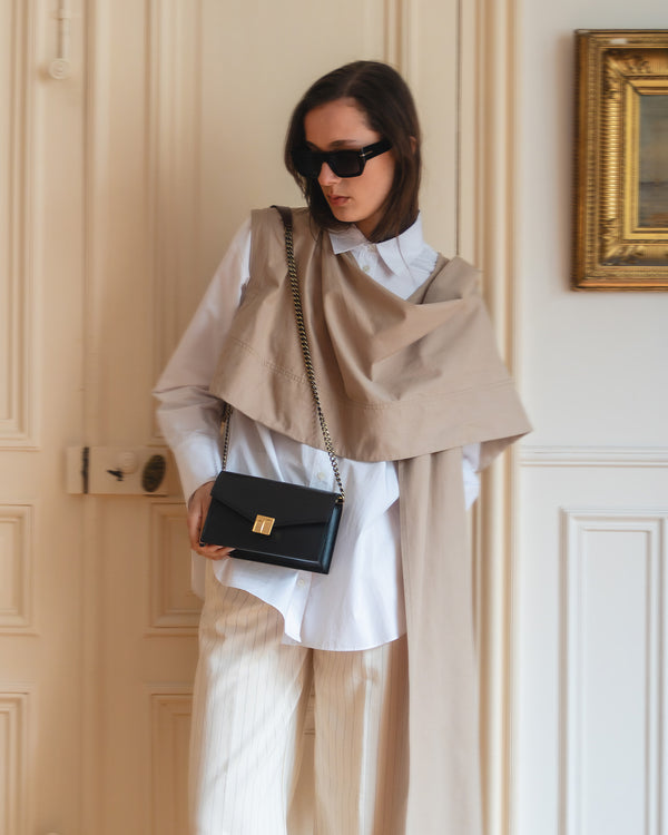 ELEANOR bag in Black worn crossbody on chain strap, held in hand, front view