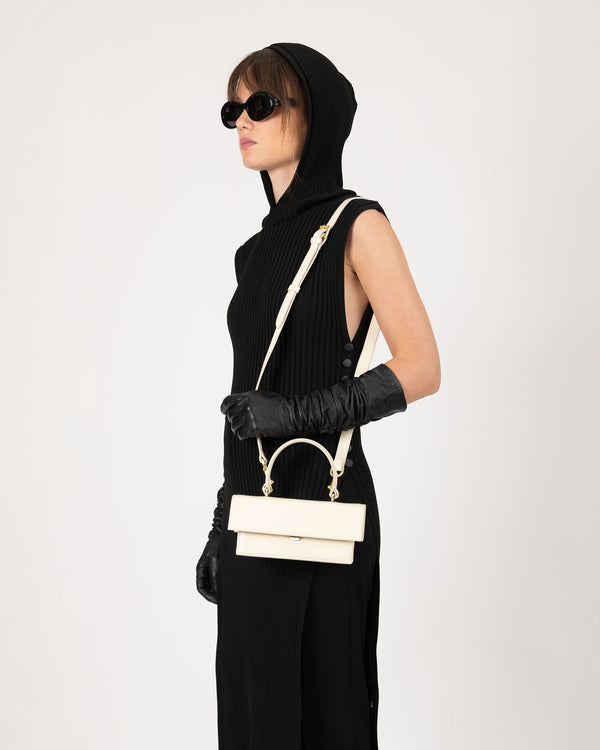 Sac THEA MINI Ivoire porté en bandoulière, vue de profil sur modèle avec gants noirs