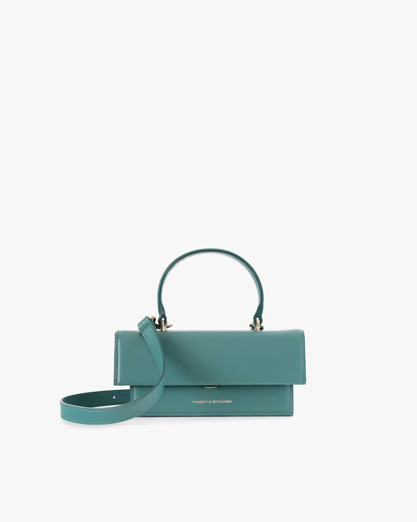 Sac THEA MINI turquoise de face, rabat fermé, anse courte relevée et bandoulière détachée posée devant