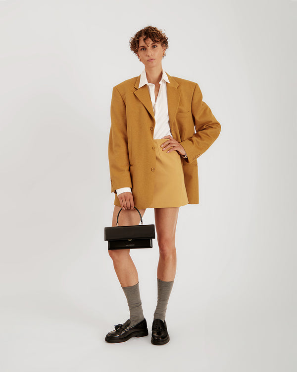 Sac THEA noir porté à la main par anse rigide, tenue oversize jaune moutarde