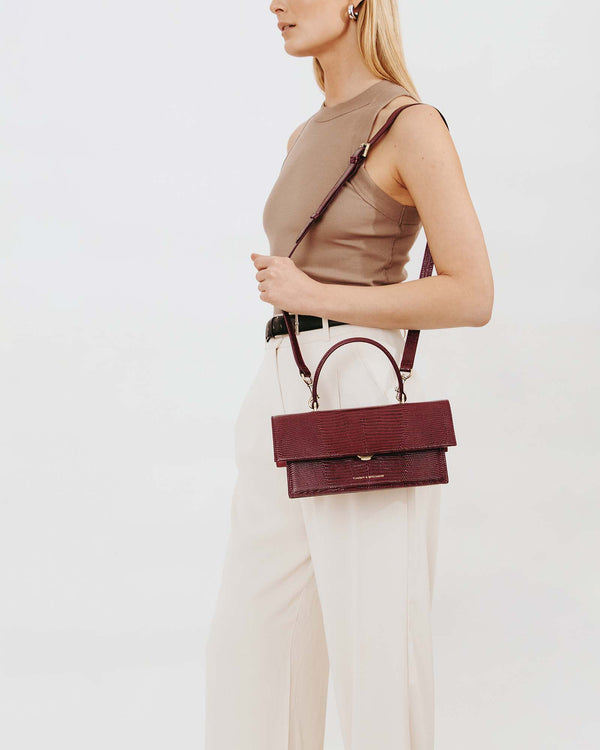 THEA bag in Bordeaux Embossed Lizard, worn crossbody, top handle visible, side view