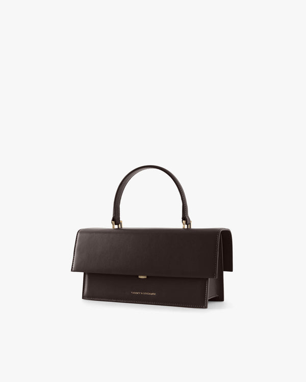 THEA bag in Chocolate, three-quarter view, flap closed, rigid handle held upright, on white background