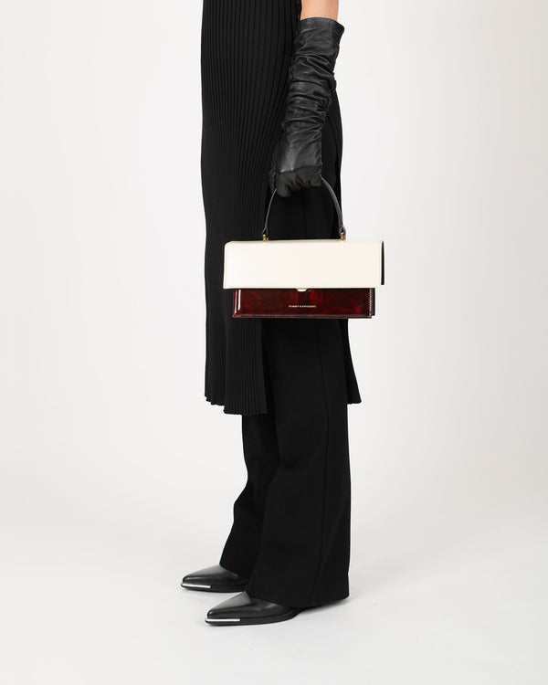 Sac THEA Colourblock art déco porté à la main par sa poignée, vue de profil, coloris écru et rouge bordeaux